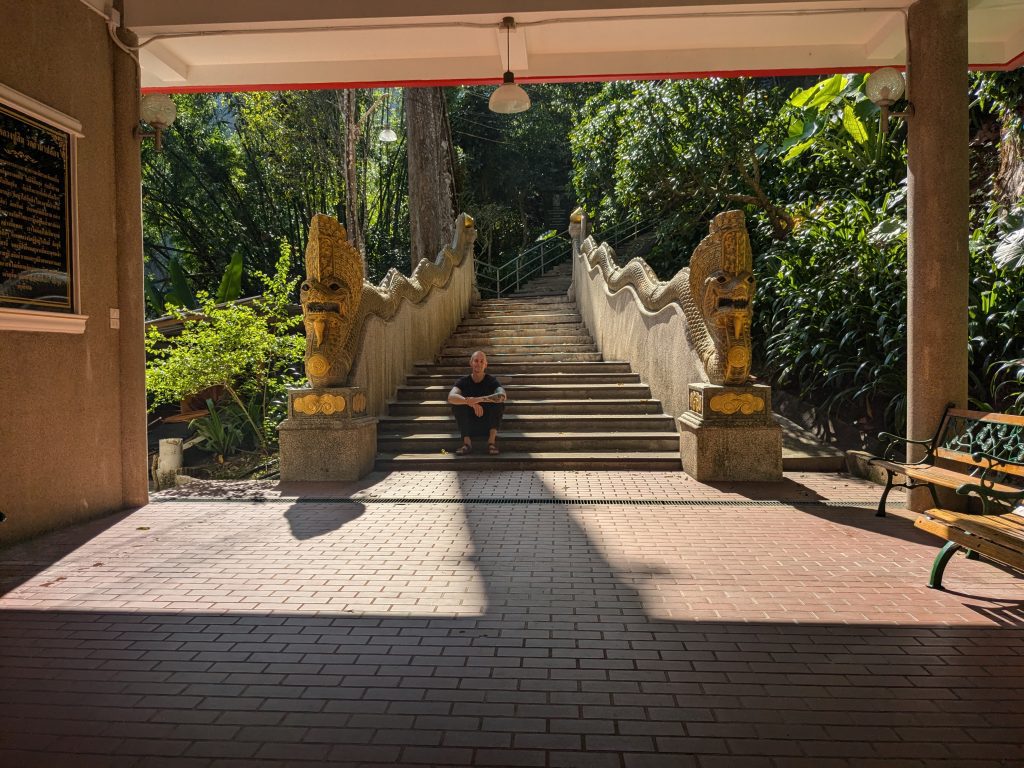 The photo shows Tommas sitting at the bottom of the stairs leading to Wat Tham Pha Plong