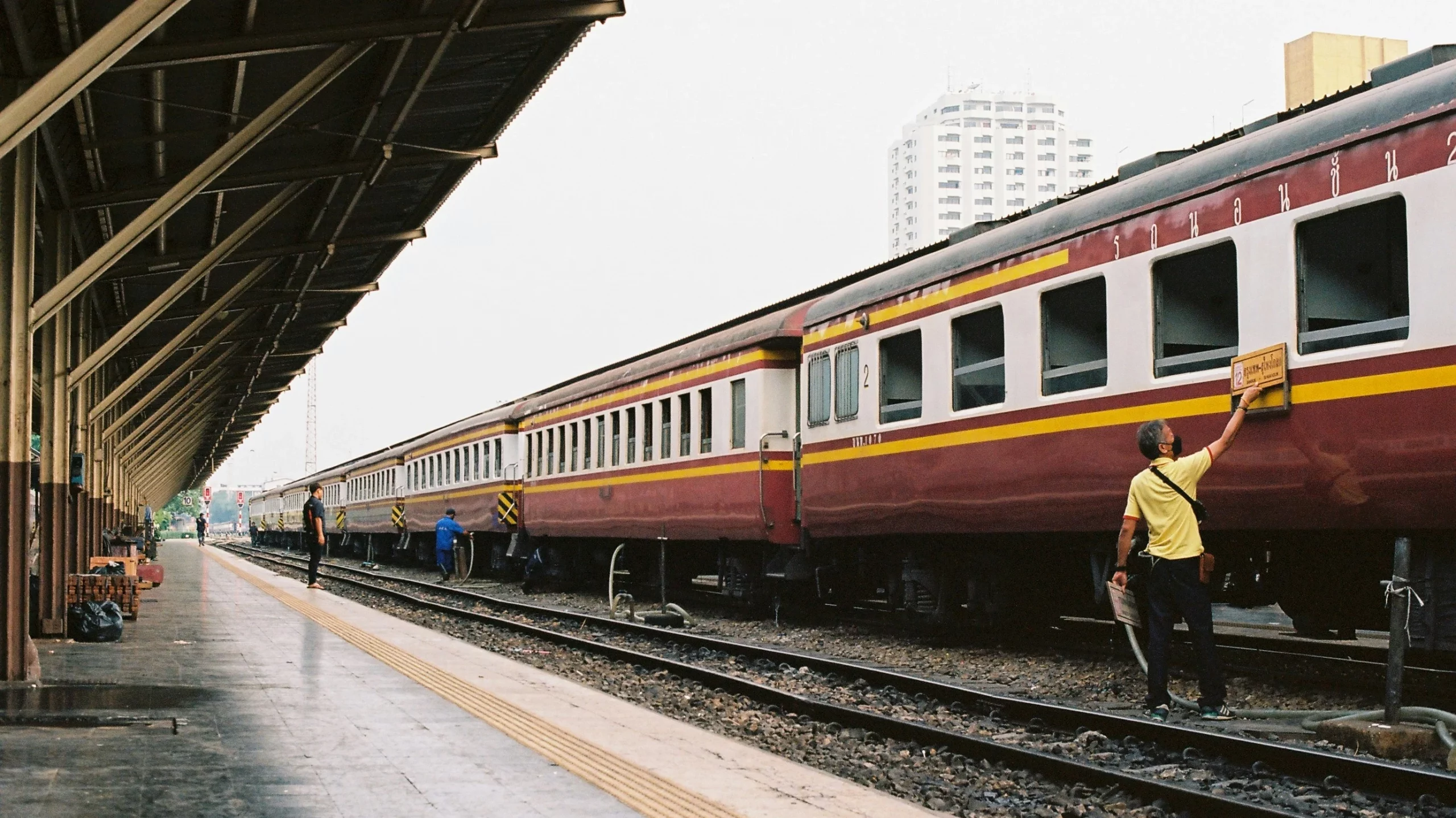 The image shows an auburn coloured sleeper train in Bangkok on a cloudy day. 
