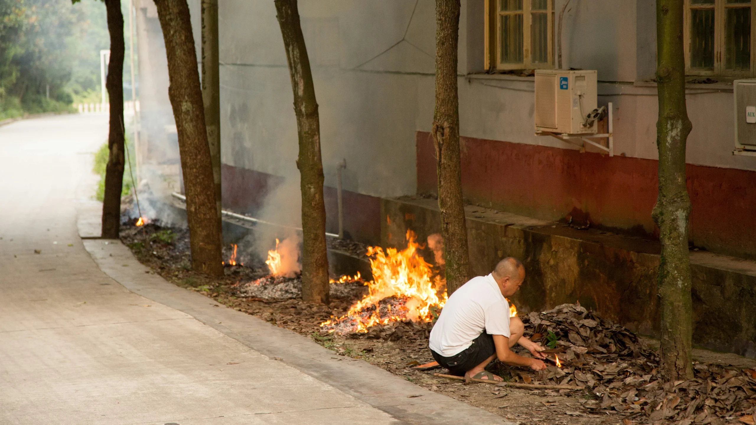 A man sitting on the side of the road and setting fire to leaves - these and similar scenes can often be observed during burning season